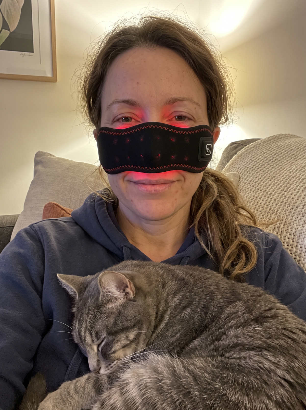 Mum on the couch, Sinuglow band on and glowing, cat asleep on her chest