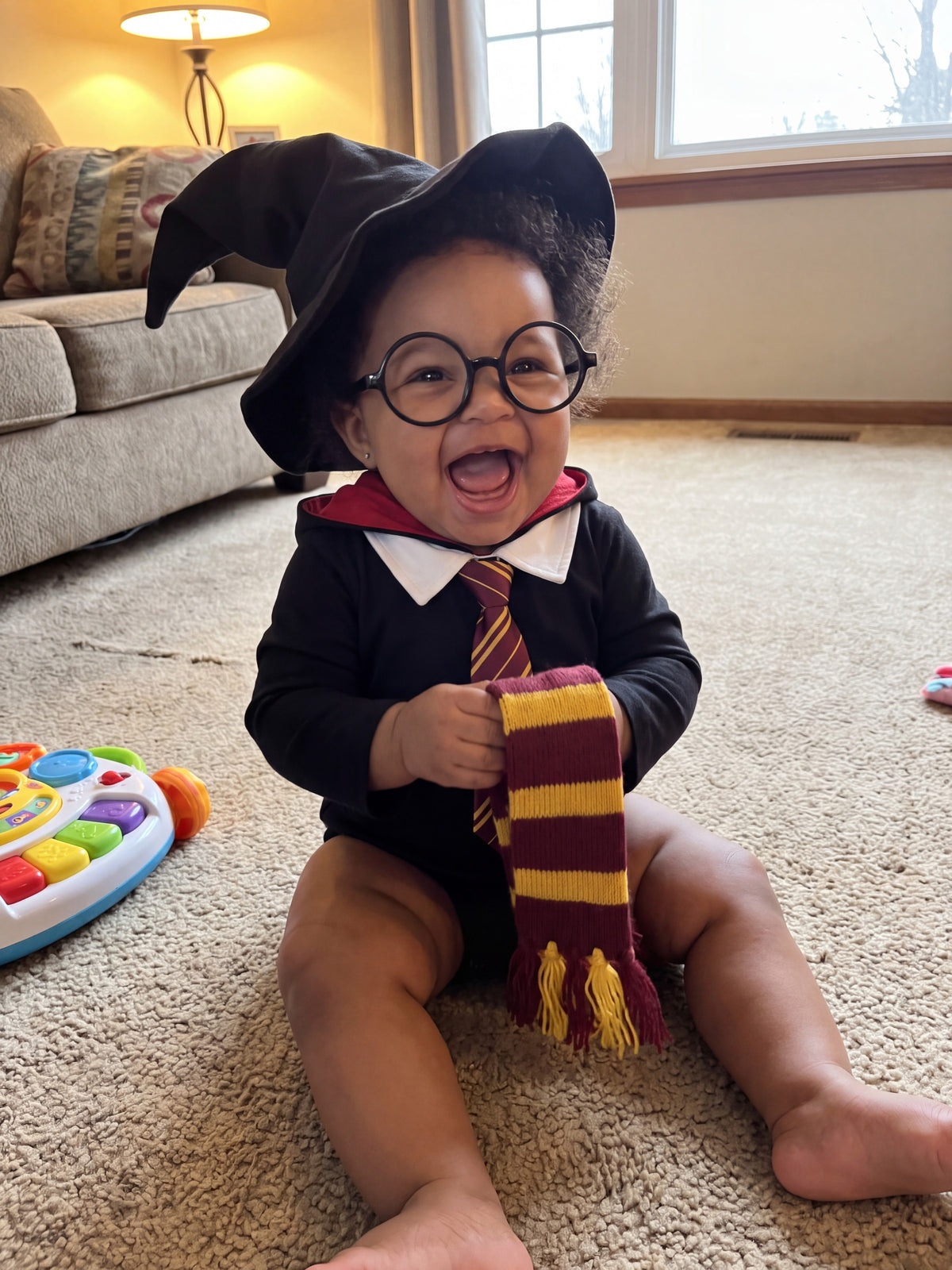 A baby girl laughing in the Wee Wizard costume on the living room floor